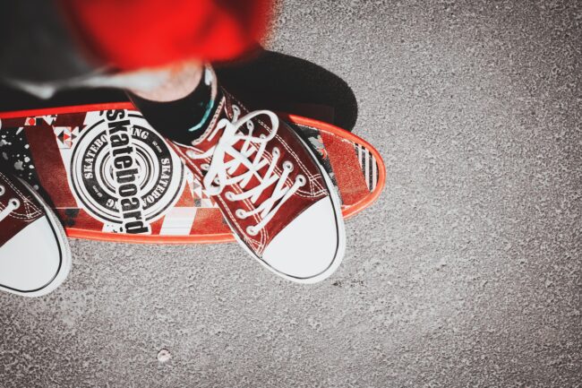 Red trainers standing on a red skateboard on tarmac, viewed from above.