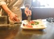 Chef prepares a dish by placing food onto a white plate in a restaurant kitchen.